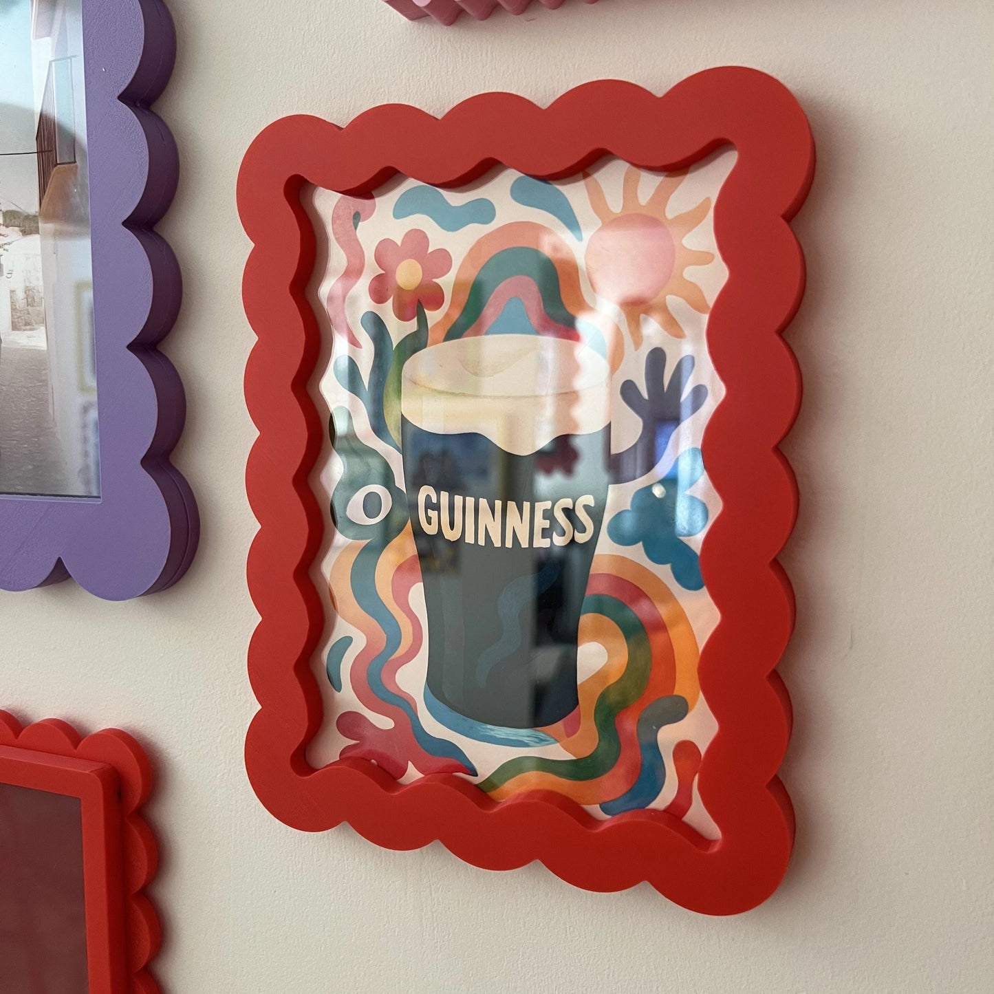 Colorful framed artwork with a Guinness beer glass design on a wall with other frames.