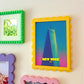 Colorful picture frames on a wall with a colorful 'New York' poster inside one of them.